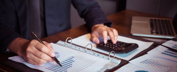 A person working on financial documents with a calculator and laptop, representing bookkeeping tasks.
