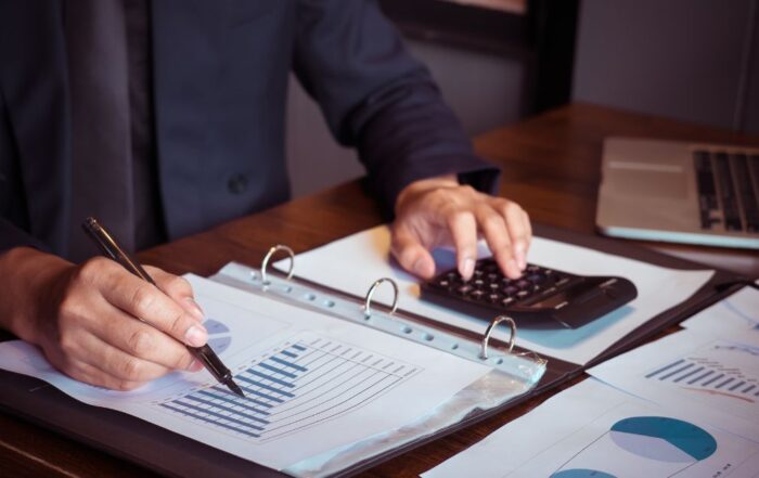 A person working on financial documents with a calculator and laptop, representing bookkeeping tasks.