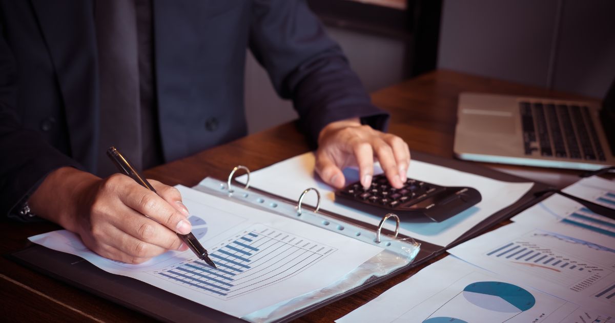 A person working on financial documents with a calculator and laptop, representing bookkeeping tasks.