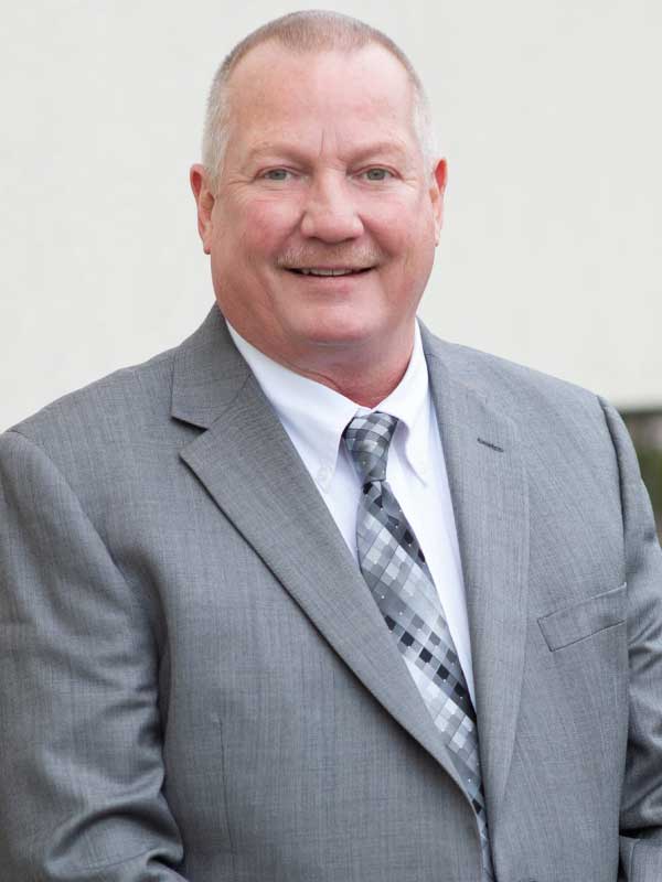 A photo of Jeff Scheeler wearing a gray suit, with a white dress shirt and patterned tie.