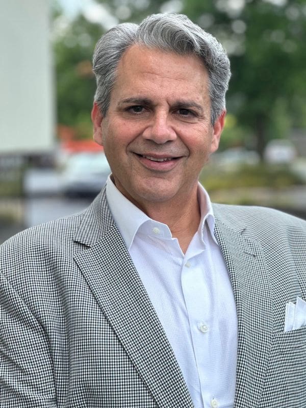 A photo of Mark A. Roger wearing a white dress shirt with a black and white jacket.