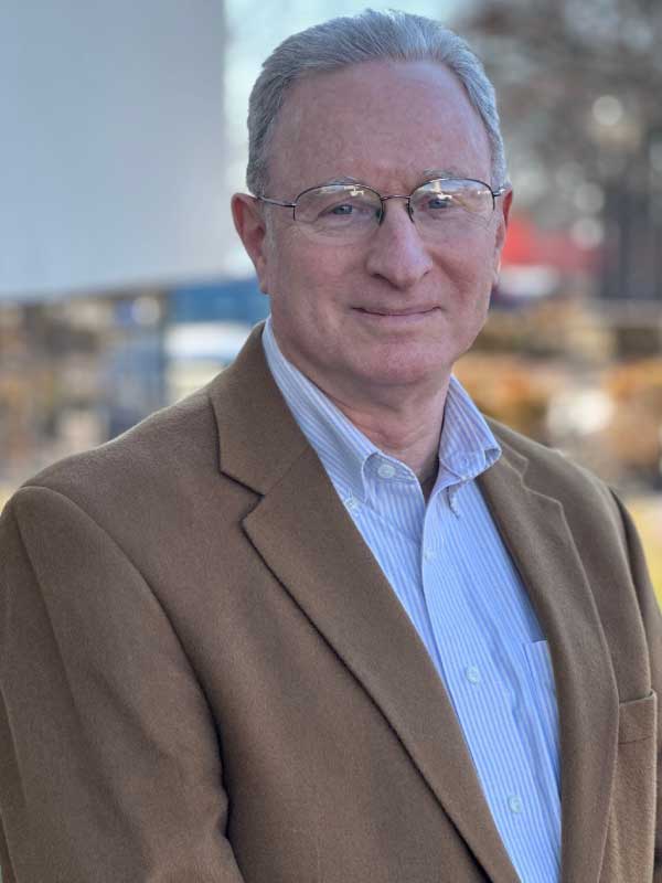 A photo of Paul Dorger wearing a light blue dress shirt with a light brown blazer outside of TP4 Advisors Office building.