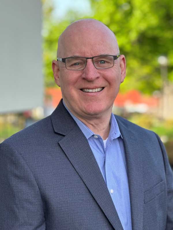 A photo of Thomas Stokes wearing a blue dress shirt with a gray suit outside the Tp4 Advisors office building.